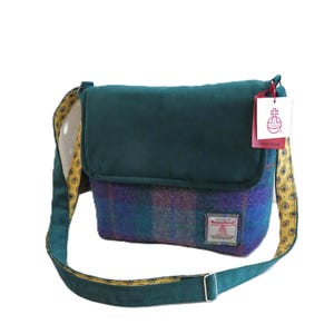 May include: A teal and plaid Harris Tweed shoulder bag with a flap closure. The bag features a teal strap with a yellow paisley pattern on the underside. A tag with a logo hangs from the top.