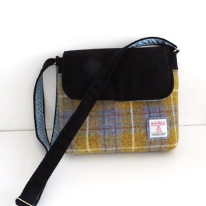 May include: A shoulder bag with a black flap and strap. The bag's body features a yellow, blue, and brown plaid pattern. The strap is black, and the interior lining is a light blue with a white polka dot pattern.