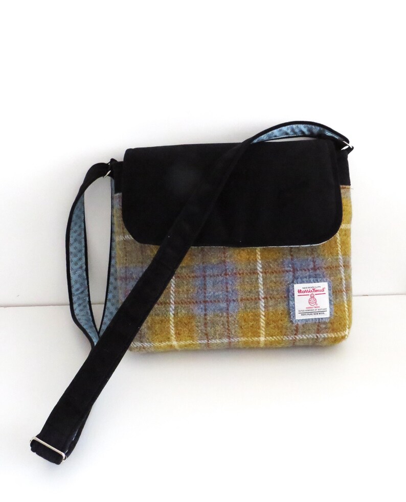 May include: A shoulder bag with a black flap and strap. The bag's body features a yellow, blue, and brown plaid pattern. The strap is black, and the interior lining is a light blue with a white polka dot pattern.