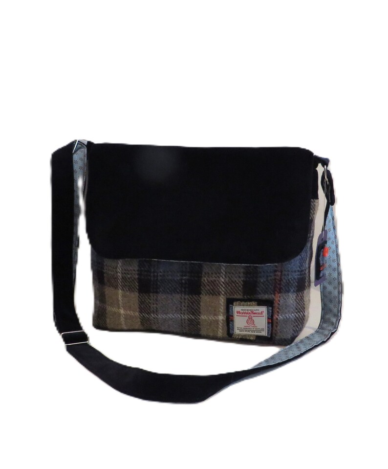 May include: A rectangular messenger bag with a black flap and strap. The main body features a plaid pattern in shades of gray, brown, and blue. A small label is sewn on the front. The bag has a blue and white patterned side.