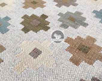 Könnte beinhalten: Ein weißer Teppich mit einem geometrischen Muster in Braun-, Grün- und Blautönen. Das Muster besteht aus sich wiederholenden Quadraten und Rauten.