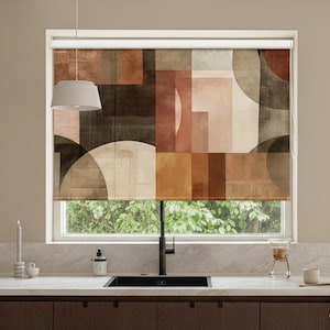 Op de afbeelding: Een raam met een geometrisch patroon in bruin-, beige- en roesttinten. Het ontwerp bevat vierkanten, rechthoeken en halve cirkels. Het raam bevindt zich boven een aanrecht met een gootsteen en kraan.