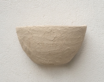 May include: A beige ceramic wall planter with a textured surface. The planter is mounted on a white wall.