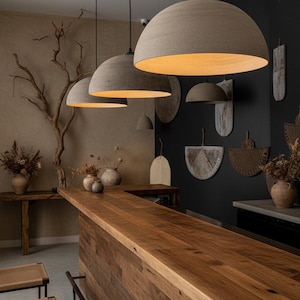May include: Interior view of a bar area featuring three large, dome-shaped pendant lights. The bar has a wooden countertop and front. Rustic decor includes wall hangings and dried floral arrangements, creating a warm atmosphere.
