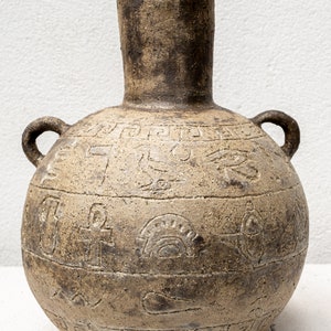 Puede incluir: Un jarrón grande de cerámica marrón con dos asas y tallas intrincadas. El jarrón tiene un cuerpo ancho y redondo y un cuello estrecho.