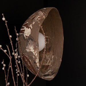 May include: A large, brown, ceramic lampshade with a white and brown abstract design. The lampshade is lit from within, casting a warm glow.