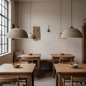 May include: Interior of a restaurant featuring wooden tables and chairs. Large, dome-shaped pendant lights hang from the ceiling. A large window is on the left side of the room, and the walls are a neutral colour.