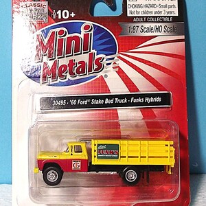 May include: A miniature yellow and red '60 Ford Stake Bed Truck, packaged in a clear plastic case. The truck features the text "FUNK'S" on the side and is a 1:87 scale model. The packaging includes the "Mini Metals" logo and a warning about small parts.