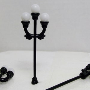 Peut inclure: Trois lampadaires en métal noir avec des globes blancs. Les lampadaires sont sur une surface blanche.