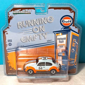 Puede incluir: Un coche modelo Volkswagen Beetle de 1966 a escala 1:43 en colores azul claro y naranja Gulf con el número 54 en el techo y las puertas. El vehículo está dentro de su embalaje blíster original con la marca y gráficos Running on Empty.