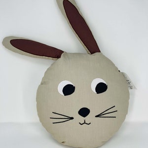 Könnte beinhalten: Ein rundes, beiges Kissen mit einem braunen Hasengesicht. Der Hase hat schwarze Augen, eine schwarze Nase und schwarze Schnurrhaare.
