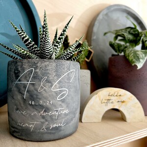 May include: A gray concrete planter with a succulent plant, featuring white script that reads "A & S", date, and "love, adventure, heart & soul". A small, arched decor piece reads "hello little one".