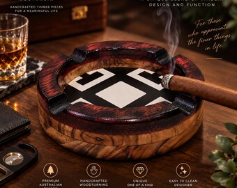 May include: A round wooden cigar ashtray featuring a dark red stained rim and a central white inlay with a black geometric pattern. A lit cigar rests in one of the four notches. The text reads CIGAR ASHTRAY, CREATIVE BURNINGS CO, and more.