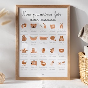 Puede incluir: Un marco de madera con el texto "Mes premières fois avec maman". La impresión presenta iconos ilustrados que representan los hitos del bebé, como los primeros pasos y el primer baño. El marco es de madera clara.