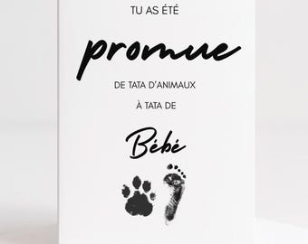 May include: A white greeting card with black text and paw and footprint graphics. The text reads "Tu as été promue de tata d'animaux à tata de Bébé."