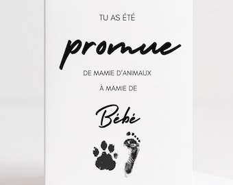May include: A white greeting card with black text and paw print and footprint graphics. The card reads "Tu as été promue de mamie d'animaux à mamie de Bébé."