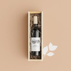 Puede incluir: Una botella de vino tinto en una caja de regalo de madera. La botella de vino tiene una etiqueta blanca con el texto "Domaine du bonheur" y una ilustraci&oacute;n de paisaje. La caja est&aacute; llena de paja.
