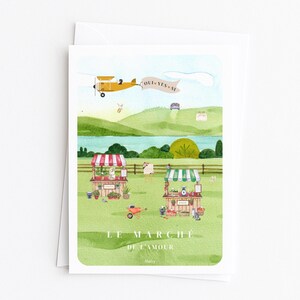 May include: A watercolour greeting card depicting a rural market scene. A yellow biplane tows a banner reading "OUI YES SI". The card features the text "LE MARCHE DE L'AMOUR" and illustrations of market stalls, fields, and a lake in a pastoral setting.