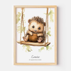 May include: A framed watercolor print features a cute hedgehog on a wooden swing. The hedgehog is brown and tan with blue eyes, holding a brown object. The print includes the name "Louise" and the date "21 septembre 2025".
