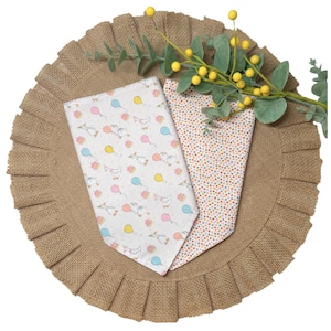 May include: Two triangular fabric pet bandanas. One features a white background with a repeating pattern of geese, pink and blue balloons, and small cakes. The second bandana has a dense, multi-colored polka dot pattern on a white background.