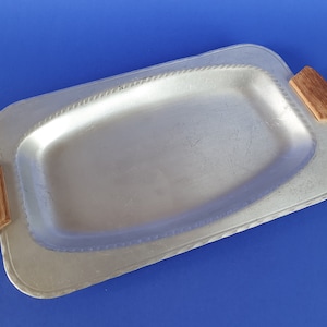 May include: A silver serving tray with two wooden handles. The tray has a slightly raised edge and a textured rim.