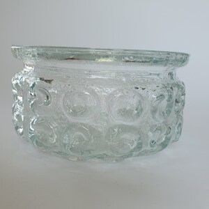 May include: Clear glass bowl with a textured, bubble-like pattern around the sides. The bowl has a slightly flared rim and a rounded shape. The glass appears to be thick and sturdy, suitable for various uses.