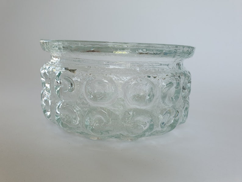 May include: Clear glass bowl with a textured, bubble-like pattern around the sides. The bowl has a slightly flared rim and a rounded shape. The glass appears to be thick and sturdy, suitable for various uses.