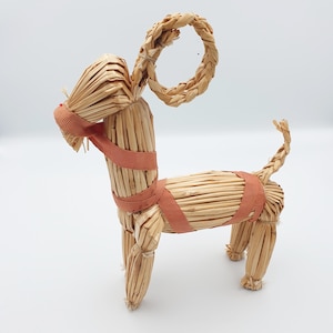 Könnte beinhalten: Eine Strohziegenfigur mit einem braunen Band um den Körper. Die Ziege hat einen Strohhschwanz und einen Strohring als Kopf.