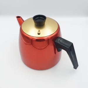 以下が含まれることがあります： 金色の蓋と黒いプラスチック製の取っ手を持つ赤い金属製のティーポット