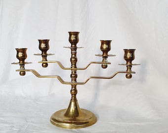 Può includere: Un candelabro vintage in ottone con cinque portacandele. Il candelabro ha una base rotonda, uno stelo centrale e bracci curvi che si estendono per sostenere le coppe delle candele. L'ottone ha una calda patina invecchiata e il design è simmetrico.