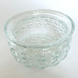 May include: A clear glass bowl with a textured, bubble-like pattern around the sides. The bowl has a rounded shape and a smooth rim. The glass is transparent, allowing light to pass through. This bowl is suitable for serving or display.