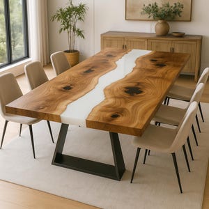 May include: A large wooden dining table with a white resin river design. The table has a dark metal base and is surrounded by six beige upholstered chairs. The table is approximately 240 cm long. The room has a neutral colour palette.