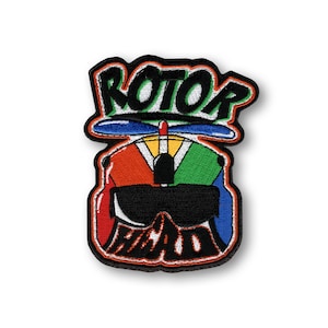 May include: Embroidered patch with the words "ROTOR HEAD" in a stylized font. The patch features a colorful design of a helicopter pilot's helmet with a propeller and goggles. The design incorporates red, orange, yellow, green, and blue.