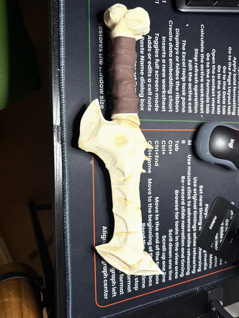 May include: A bone-colored, fantasy-style dagger with a brown wrapped handle. The blade has a textured surface and a stylized design. The dagger is lying on a black surface with computer-related text and a mouse.