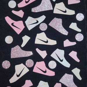Może przedstawiać: Czarne tło z r&oacute;żowymi, białymi i beżowymi błyszczącymi butami sportowymi. Buty są rozrzucone losowo na tle. Niekt&oacute;re buty mają marmurowy wz&oacute;r.