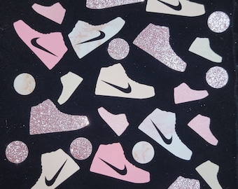May include: A black background with pink, white, and beige glitter sneakers. The sneakers are scattered randomly on the background. Some of the sneakers have a marble pattern.