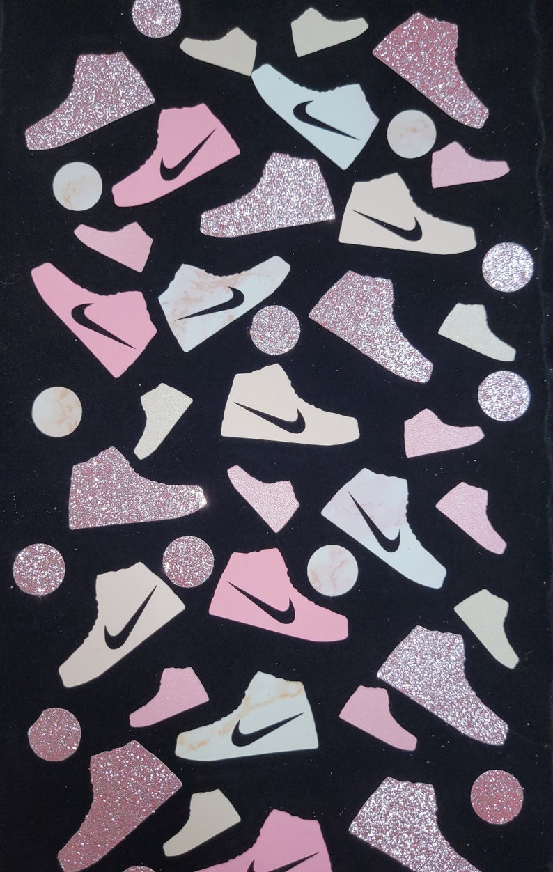 Może przedstawiać: Czarne tło z r&oacute;żowymi, białymi i beżowymi błyszczącymi butami sportowymi. Buty są rozrzucone losowo na tle. Niekt&oacute;re buty mają marmurowy wz&oacute;r.