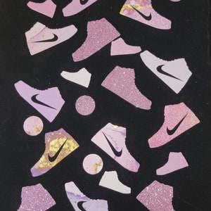 Może przedstawiać: Czarne tło z r&oacute;żowymi i białymi błyszczącymi butami rozrzuconymi po powierzchni. Buty mają białe logo swoosh.