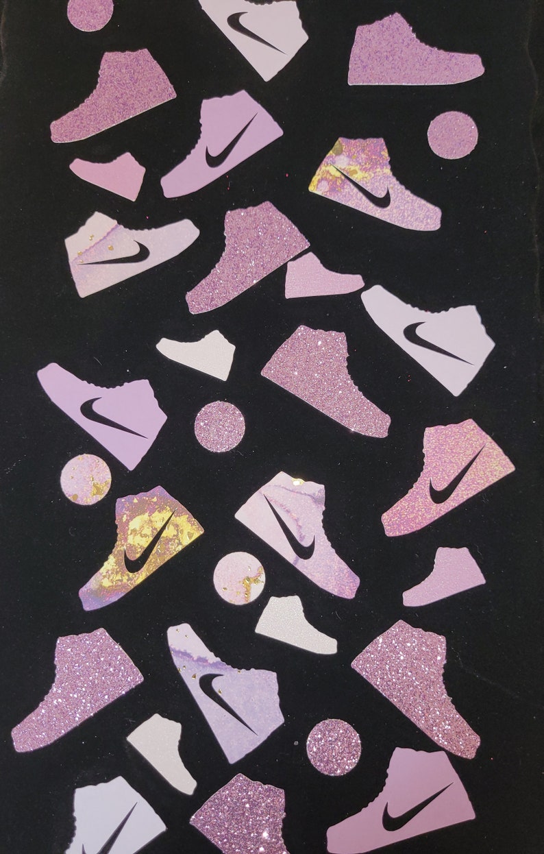 Może przedstawiać: Czarne tło z r&oacute;żowymi i białymi błyszczącymi butami rozrzuconymi po powierzchni. Buty mają białe logo swoosh.