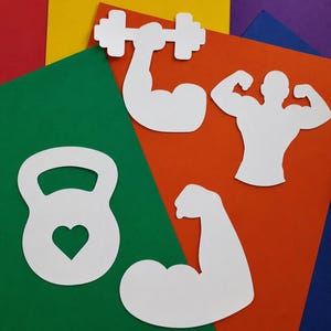 May include: Four white paper cutouts featuring fitness-themed shapes: a kettlebell with a heart-shaped cutout, a flexed arm holding a dumbbell, a muscular torso with both arms flexed, and a single flexed arm, all arranged on colorful paper sheets.
