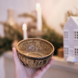 Puede incluir: Un pequeño cuenco de cerámica marrón y amarillo con una superficie texturizada. El cuenco se sostiene en una mano.