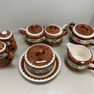 Puede incluir: Un juego de seis piezas de cocina de cerámica con un patrón de veta de madera y acentos florales. El juego incluye dos pequeños saleros y pimenteros, dos platos pequeños cubiertos, una jarra de crema y una mantequillera.