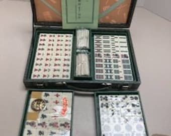 Puede incluir: Un juego de mahjong vintage en una maleta de transporte verde con un diseño blanco y rojo. El juego incluye 144 fichas, dados y un conjunto de instrucciones en japonés.