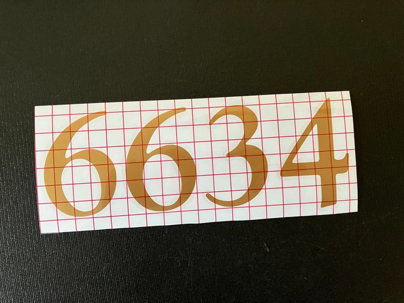May include: Gold vinyl numbers 6634 on a white gridded backing.