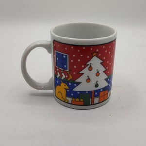 May include: White ceramic mug with a Christmas scene. The scene features a red background with white polka dots, a blue and white house, a white Christmas tree with orange and green ornaments, and a yellow dog.