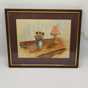 Antique painting depicting a table with a blue vase, a pink lamp and a red book
