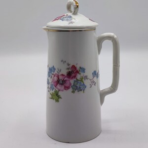 Peut inclure: Une crémier en porcelaine blanche avec un motif floral dans des tons de rose, bleu et vert. La crémier a un couvercle avec une bordure dorée et une poignée de style bambou.