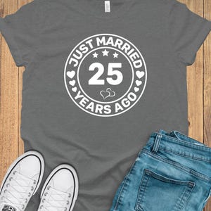 May include: A gray t-shirt with the text "JUST MARRIED 25 YEARS AGO" in a white circular design. The image also shows blue jeans and white sneakers.