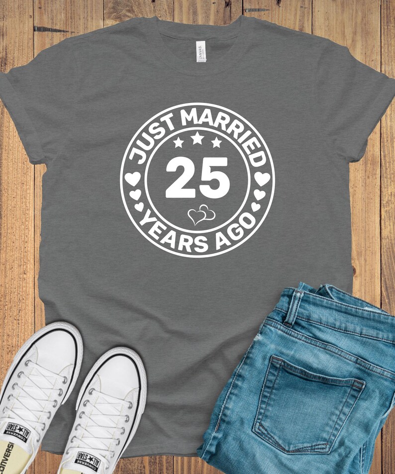 May include: A gray t-shirt with the text "JUST MARRIED 25 YEARS AGO" in a white circular design. The image also shows blue jeans and white sneakers.