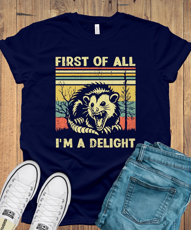 May include: A navy blue t-shirt with a vintage-style graphic of a possum with the text "First of all I'm a delight".